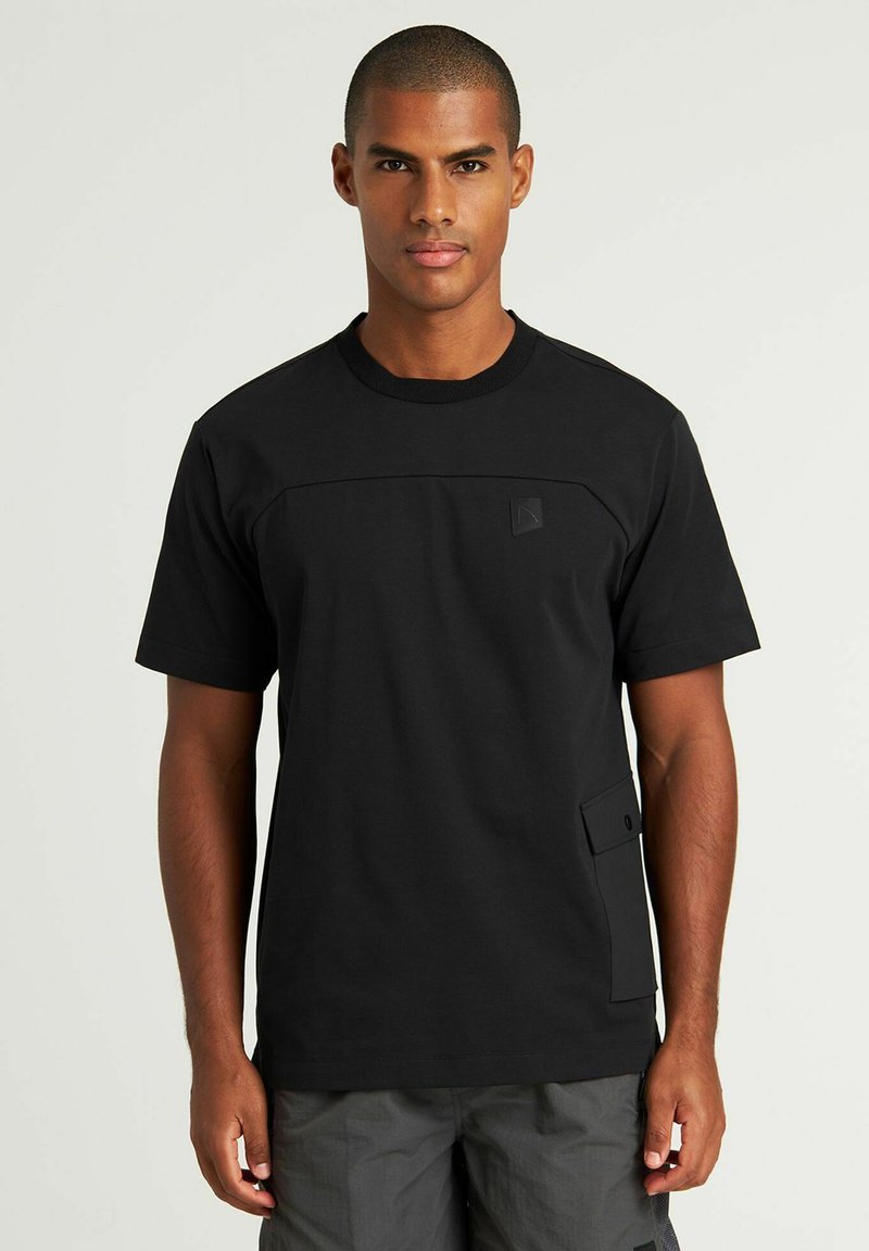 T-shirt nera a maniche corte con scollatura a girocollo, che presenta un pannello testurizzato sul petto e una tasca laterale con chiusura a bottone.