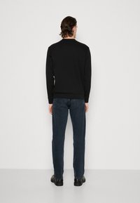 Sudadera negra de manga larga, con cuello redondo y puños acanalados, combinada con jeans azul oscuro y zapatos negros. Textura suave, ajuste casual.