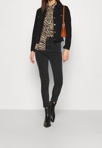 Schwarze Denimjacke über einem braunen Zebra-Print-Shirt, kombiniert mit schwarzen Skinny-Jeans und schwarzen Stiefeletten. Braune Handtasche mit silbernen Akzenten.