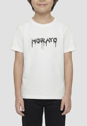 Enfant portant un t-shirt blanc à manches courtes avec un texte noir dégoulinant "MORATO" et un pantalon noir sur un fond gris uni.