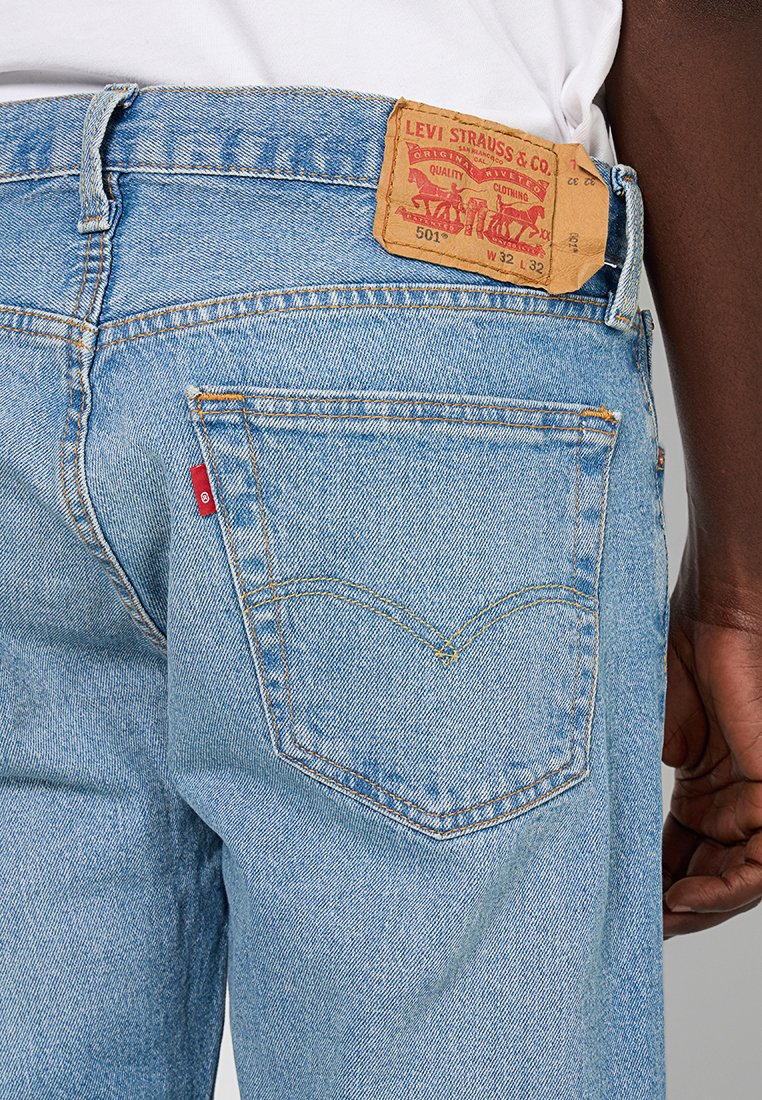 Helleblaue Denim-Jeans mit klassischem geraden Schnitt. Die Gesäßtasche verfügt über gelbe Nähte und ein rotes Levi's-Label. Abgeriebenes Material.