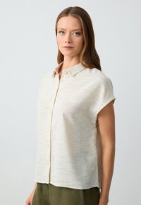 Camicetta a maniche corte con bottoni in lino beige chiaro, dotata di una texture sottile, con colletto classico e vestibilità relaxed.