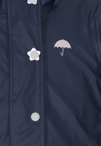 Jūros mėlynumo atsparus vandeniui švarkas su sidabro žvaigždėmis ir skėčių akcentais, lygia tekstūra, snapeliais užsegamas ir siūlėmis siuvinėjamas.