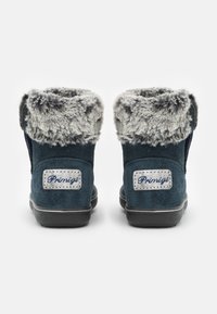 Tmavě modré semišové boty s šedým umělým kožíškem na límci, s logem na patě. Gumová podrážka a prošívané detaily podél designu.