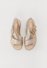Metallic gold sandals with crisscross straps and a side buckle. Smooth texture, open heel, and cushioned insole for comfort.