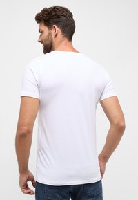 Hvid bomulds t-shirt med korte ærmer, rund halsudskæring, glat struktur og tætsiddende silhuet, båret med mørkeblå jeans.