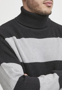 Sweter z golfem o fakturowanym splocie z czarno-szarymi poziomymi paskami. Materiał jest gruby, ryżowy i miękki w dotyku.
