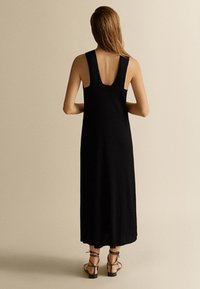 Robe maxi noire à côtes avec des bretelles larges, un dos échancré et une coupe décontractée, portée avec des sandales à lanières.