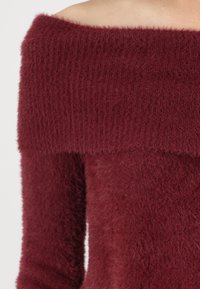 Top en tricot bordeaux à épaules dénudées avec une texture côtelée et un tissu doux et moelleux. Manches longues avec une coupe décontractée.