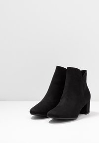 Černé semišové kotníkové boty s špičatou špičkou a středním blokovým podpatkem. Exteriér je hladký, bez viditelných vzorů nebo kovových prvků.