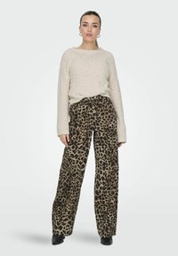 Maglione beige lavorato a maglia con polsini a coste abbinato a pantaloni larghi in stampa leopardata con un dettaglio annodato sul davanti e una texture in tessuto liscia.