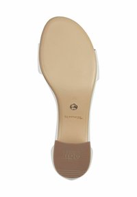 Tan gummisula med texturerat mönster; beige fotbädd; vit ovandel med minimalistsk design; märkeslogotyp nära hälen. Storlek 37.
