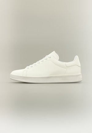 Baskets basses blanches minimalistes avec lacets, tige en cuir lisse et semelle en caoutchouc texturée, présentées sur un fond neutre.