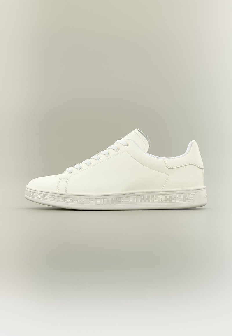 Baskets basses blanches minimalistes avec lacets, tige en cuir lisse et semelle en caoutchouc texturée, présentées sur un fond neutre.