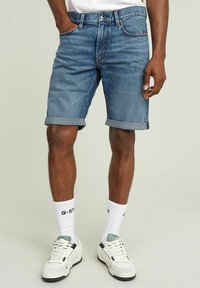 Shorts en denim avec un délavage bleu clair, des coutures contrastées, des ourlets retroussés et cinq poches. Associés à des chaussettes blanches et des baskets.