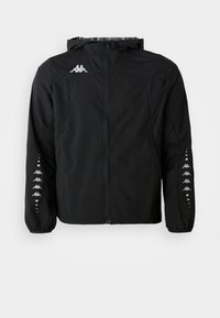 Sort letvægtsjakke lavet af nylon med lynlås foran, hætte og elastiske manchetter. Har et logo på brystet og mønstrede detaljer på ærmerne.
