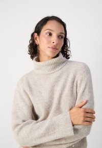 Lys beige høyhalset genser med ribbestrikket tekstur og lange ermer, med en avslappet passform og mykt, lunt materiale.