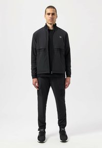 Black athletic jacket with a high collar, mesh side panels, and a zip closure. Paired with matching black jogger pants featuring cargo pockets.