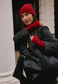 Sac cabas en cuir noir avec une boucle en argent, assorti à un blazer gris texturé, un bonnet rouge en maille et des gants sans doigts.