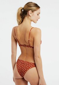 Bruin gebloemd bikini met dunne bandjes, voorzien van een geribbelde textuur en kleine witte bloemenpatronen. De onderkant heeft een medium hoge snit.
