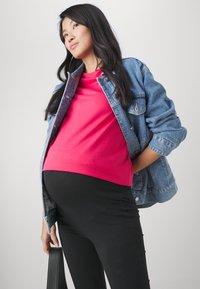 Zwangerschapsoutfit met een roze t-shirt, spijkerjack en zwarte legging. De stof lijkt glad, met een relaxte pasvorm en een casual ontwerp.
