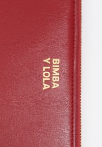 Billetera de cuero rojo con el texto dorado en relieve "BIMBA Y LOLA" y un cierre con cremallera con costura dorada a lo largo del borde. Textura suave.