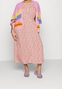 Květinové midi šaty s růžovým pleteným cardiganem, který má žluté, modré a červené pruhy. Fialové sandály na podpatku doplňují outfit.