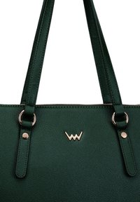 Dunkelgrüne Kunstleder-Tote-Bag mit zwei Schulterriemen, goldfarbener Hardware und geprägtem Logo auf der Vorderseite. Strukturierte Oberfläche.