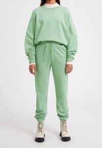 Ensemble sweat-shirt et pantalon de survêtement vert menthe en tissu doux avec poignets côtelés. Assorti à des bottes à lacets de couleur claire avec semelles noires.