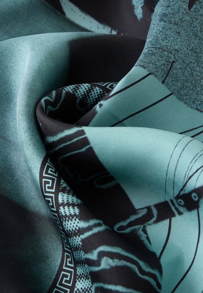 Gros plan sur un tissu plié bleu sarcelle et noir avec des motifs géométriques et abstraits dans une texture lisse et légèrement brillante.