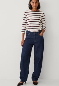 Gestreepte langwerpige blouse in crème en bordeaux, gecombineerd met losse donkerblauwe jeans. Bevat een hoge taille en klassieke zakken.