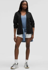 Czarna lekka kurtka z wysokim kołnierzem i podkreśloną talią, zestawiona z niebieską bluzką, białymi szortami i białymi trampkami. Gładka faktura materiału.