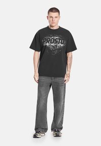 Czarny bawełniany t-shirt z teksturowanym białym wzorem graficznym i logo. Połączony z szarymi jeansami i wielokolorowymi sportowymi trampkami.