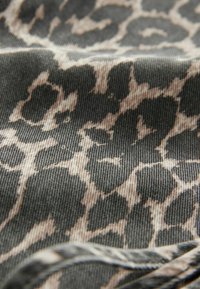 Gros plan d’un tissu doux avec un motif léopard gris foncé et beige et une texture côtelée visible.