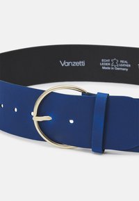 Blauwe leren riem met een ronde goudkleurige metalen gesp, met een gladde textuur en meerdere gaatjes voor aanpassingen. Aan de binnenkant staat de merknaam.
