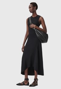 Abito midi nero a coste con orlo asimmetrico, abbinato a sandali neri flat con hardware dorato e una borsa nera morbida.