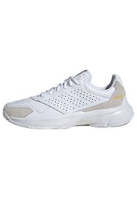 Chaussure de sport blanche avec tige en cuir perforé et accents en suède beige. Dispose d'un col rembourré, de lacets et d'une semelle texturée.