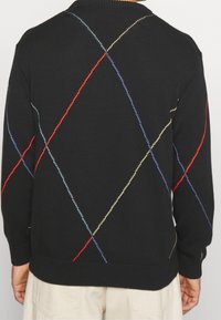 Černý pletený svetr s diamantovým vzorem v červené, modré a žluté barvě na zadní části. Hladké manžety a lem.