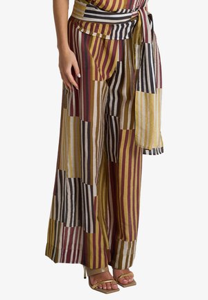 Pantaloni a gamba larga con righe verticali multicolor e cintura annodata, indossati con sandali beige con tacco alto e punta aperta.