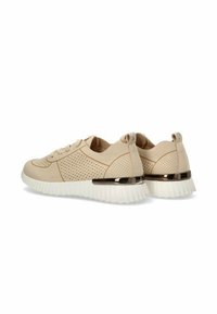 Zapatillas beige con textura perforada, diseño con cordones, detalle metálico en el talón y suela de goma blanca con estrías.
