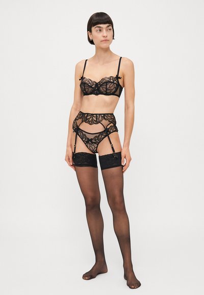 Ensemble de lingerie en dentelle noire comprenant un soutien-gorge transparent et une ceinture porte-jarretelles taille haute. Broderies florales délicates avec des bretelles ajustables et des accents en métal doré.