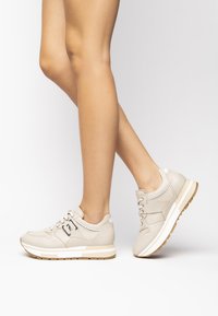 Sneakers atletici beige con dettagli bianchi, tomaia testurizzata, design con lacci e suola imbottita con fondo in gomma marrone.