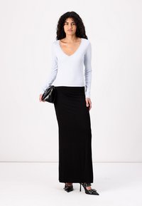 Light blue long-sleeve top with a scalloped V-neck, paired with a black fitted maxi skirt and pointed black stilettos. Holding a black handbag.