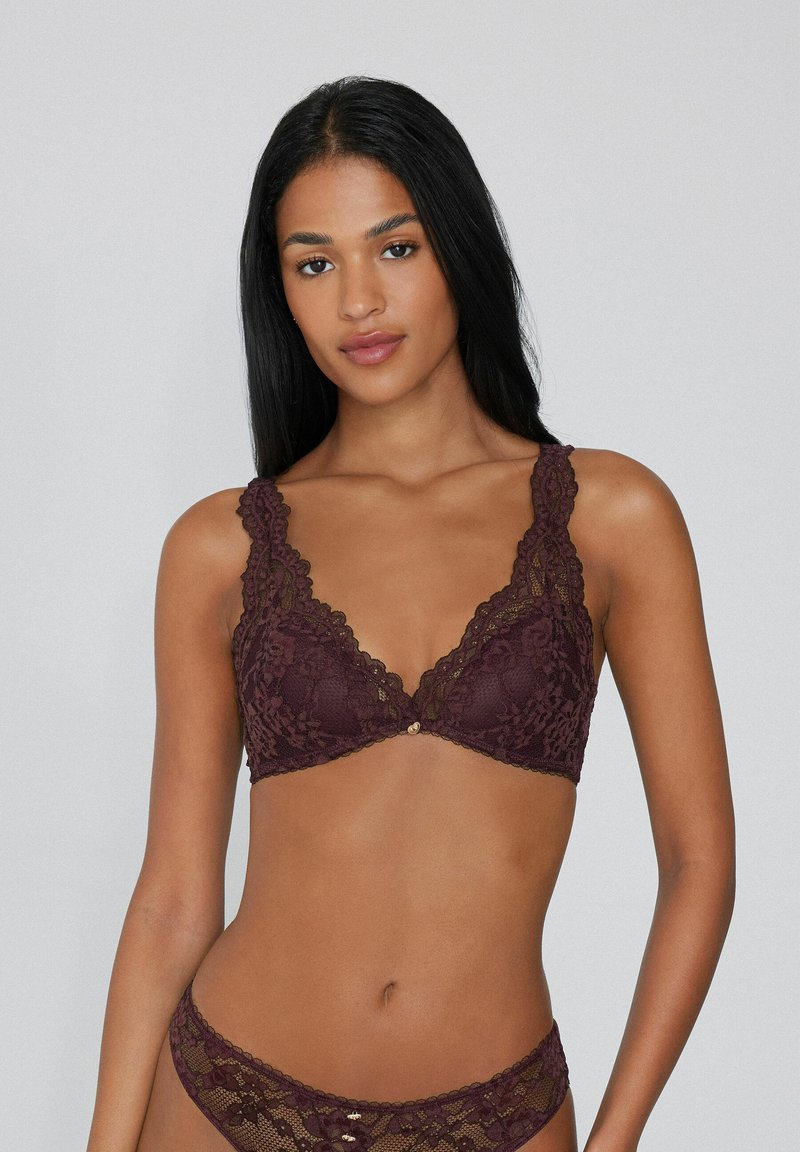 Burgunderfarbene Spitzen-Bralette mit gewellten Kanten, tiefem V-Ausschnitt und goldfarbenen Akzenten. Weicher Stoff mit floralem Muster und verstellbaren Trägern.