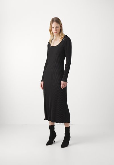 Rochie midi neagră cu tivuri, cu mâneci lungi, decolteu pătrat și detalii cu nasturi pe umeri. Asortată cu botine negre până la glezne.