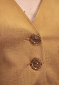 Tela de lino color mostaza con una textura suave, que presenta dos botones grandes semi-transparentes y un diseño limpio y envolvente.