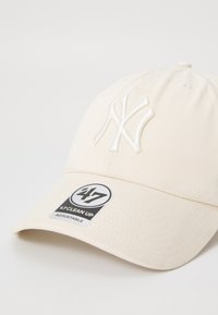 Hvid kasket med broderet NY-logo, struktureret form og justerbar rem. Har et tekstureret stof og et rundt 47-mærke på skyggen.