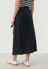 Black, flowy maxi skirt with a drawstring waist. Made from lightweight fabric, features a simple, clean design and a smooth texture.