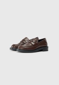 Mocassins en cuir marron avec un bout arrondi et une bande cousue sur le dessus. Ils présentent une semelle plateforme noire basse pour plus de stabilité.