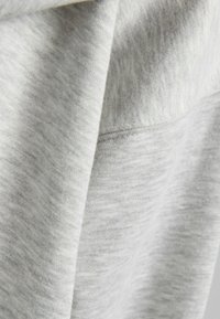 Tejido de sudadera gris claro, texturizado con un acabado suave y ligeramente difuso. Presenta variaciones sutiles en la tonalidad y un diseño simple.